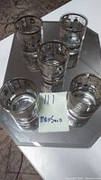 Photo showing five vintage lowball whiskey glasses with gold rim and Old World map design placed on a mirrored surface