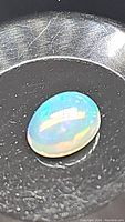 Close-up photo of a polished oval cabochon Ethiopian opal with visible play-of-color in a black tray.
