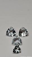 Three natural trillion cut aquamarine gemstones photographed on a plain background, showing clarity and cut precision.