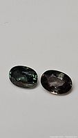 Photo showing two oval sapphire gemstones, one green and one champagne.