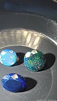 Three polished black opal stones of varied colors and patterns on a black surface.