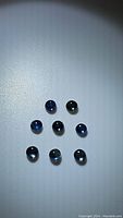 Photo of nine small round cabochon blue sapphires arranged loosely on a white surface under spotlight, showing various shades of blue and reflective surfaces.