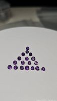 Top view of 22 round brilliant cut Brazilian amethyst gemstones neatly arranged on white background, showing size and color consistency