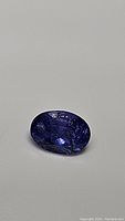 Oval cut natural tanzanite gemstone, showing deep blue purple coloration and surface inclusions from different angles.