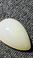 Close-up image of a pear-shaped translucent white opal cabochon exhibiting play of color on textured black surface