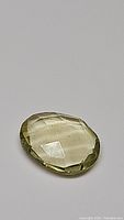 Oval fancy cut lemon citrine gemstone on a flat surface, showing pale yellow-green translucency.
