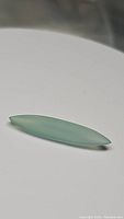 Single elongated marquise cut natural glacier blue-green chalcedony gemstone placed on white surface showing translucent blue-green color and smooth polished finish.