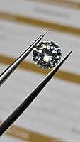 Close-up photo of a round brilliant moissanite gemstone held with tweezers showing clear facets and brilliance.