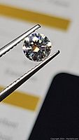 Close-up image of the round 5mm moissanite gemstone held in metal tweezers showing brilliance and fire.