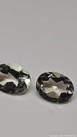 Pair of two natural oval cut green amethyst/prasiolite gemstones placed side by side on neutral background showing facets and color.