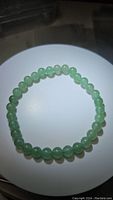 Top view of a bright green Aventurine bead stretchy bracelet laid on a round white surface, showing uniformly round polished beads.