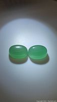 Two polished, matching oval green onyx gemstones placed side by side under direct lighting showing their translucent, green coloration and smooth finish.