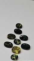 Photo showing eight oval cut green tourmaline gemstones in varying shades of green on a plain background for clear visibility of color and cut.