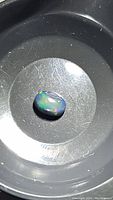 A loose oval cabochon jet black Ethiopian opal showing multicolored rainbow flashes under light.