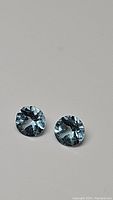 Close-up photo of the pair of round sky blue topaz gemstones showing the diamond cut facets and clarity from the top view.