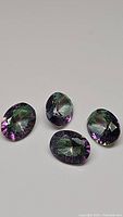 Four calibrated oval cut mystic topaz gemstones shown on a white background highlighting their purple and rainbow color effect.