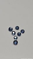 Seven natural blue sapphires shown from above on a neutral background, showcasing color and round cut.
