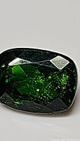 Close-up image of cushion cut Chrome Diopside showing faceting and green color.