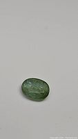 Close-up photo of natural oval cut emerald gemstone on white background showing shape and color.