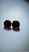 Pair of round, faceted garnet stones showing deep cherry red color and light reflections under light.