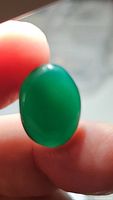 Close-up photo of an oval cabochon green onyx held between fingers, showing rich green color and smooth polished surface.