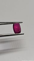 Photo of natural cushion cut ruby held by tweezers showing deep red color and clarity characteristics.