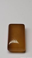 Rectangular cabochon cut yellow onyx gemstone showing polished top surface with reflection light spot.