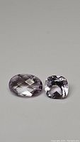 Photo showing two natural pink amethyst gemstones: one oval checkerboard cut and one cushion cut, both light pink with good clarity.