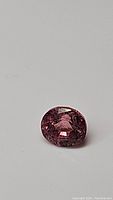 Close-up of oval cut natural pink tourmaline gemstone, showing color and faceting.