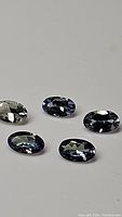 Five oval faceted multicolored tanzanite gemstones, showing colors from blue to green with high clarity and luster.
