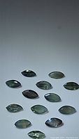 Thirteen marquis cut natural alexandrite gemstones on white background showing green-yellow hues and reflective facets.