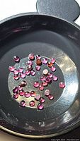 Close-up photo of multiple small round rhodolite garnet cabochons in a black tray, showing pinkish-red color and smooth domed cut.