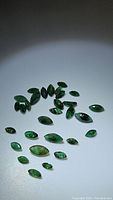 Multiple marquis cut green emerald gemstones arranged on white background under spotlight lighting.