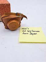 Leather carrying case for the spy camera with embossed 'Hit' logo, alongside handwritten note describing the item as 1950's Hit Spy Camera from Japan.