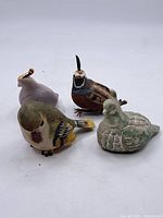 Four assorted ceramic bird figurines on white background showing variety in color and style