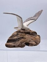 Side view of the seagull figurine mounted on a textured piece of driftwood showing natural wood grain and detailed seagull features.