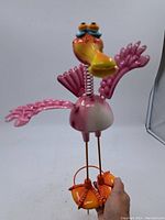 Front view of pink flamingo garden decoration showing spring neck, spread wings, orange shoes, and metal stakes.