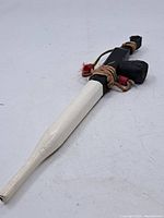 Side view of the entire ceremonial pipe showing white mouthpiece, black wooden stem, and leather with feather decorations.