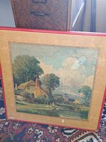 Front view of the folding table showing the scenic countryside print with trees, houses, and water under glass or clear surface with a red border frame.