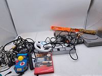 Items shown: Sony PlayStation Classic console, PlayStation controllers, Namco joystick, Wii steering wheel, orange camo accessory, power strip, and cables.
