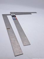 Full view of two aluminum framing squares placed in an L shape on a white surface showing their size and condition.