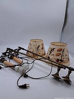 Two vintage wall mounted lights with brass hardware and wooden arms laid on floor with floral fabric lampshades and cords visible.