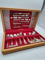 Full view of the Rogers flatware set in wooden case with red fabric lining, showing knives mounted on underside of lid and forks, spoons in slots in base.