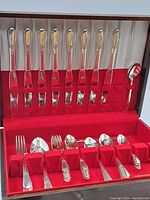 Full set of Rogers flatware displayed in a red velvet-lined case showing 8 knives, 8 forks, 7 spoons, and 1 serving spoon.