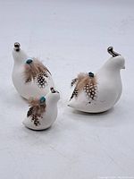 Full view of the set of three white bird figurines with feathers and metallic knobs on heads displayed on a white surface.