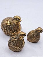 Three brass bird figurines arranged together showing different sizes and feather detail