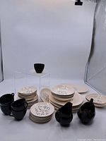 Full view of entire set showing stacked plates, multiple saucers, and two black creamer pitchers