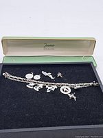 Complete lot showing the sterling silver charm bracelet with multiple charms displayed inside the original jewelry box with black velvet lining.