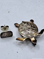 Photo of the sterling silver turtle pendant and one earring showing detailed shell texture and surface design
