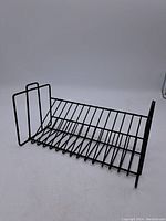 Full view of the black metal wire rack showing its rectangular shape, slanted bars for storage, and vertical side supports.